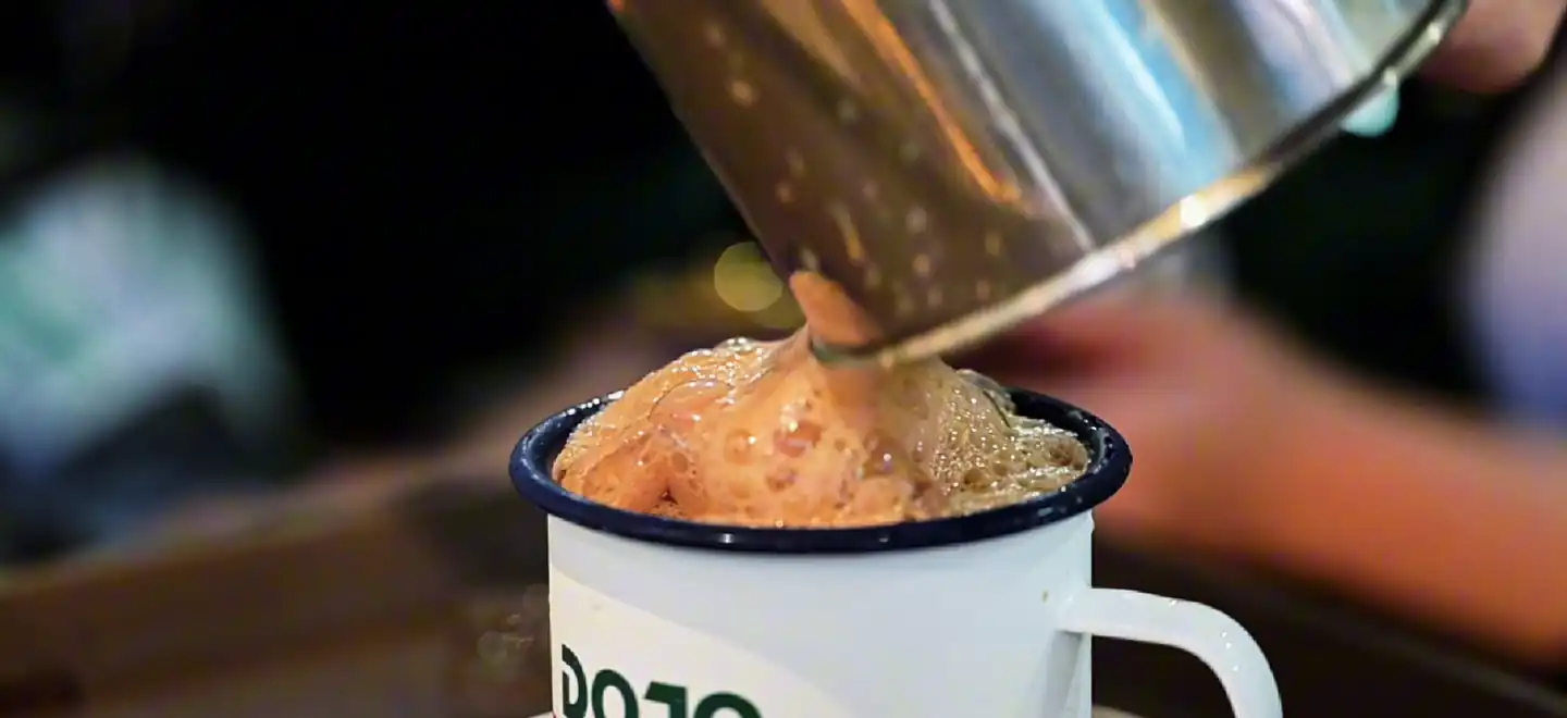 Kopi foam spilling over a DOJO enamel mug