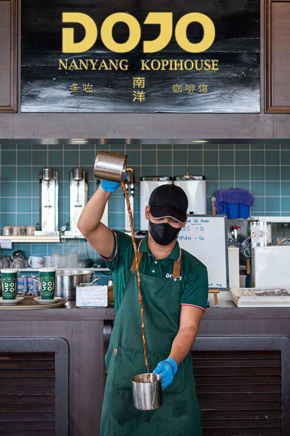 A DOJO barista pulls kopi from a height under the DOJO Nanyang Kopihouse sign